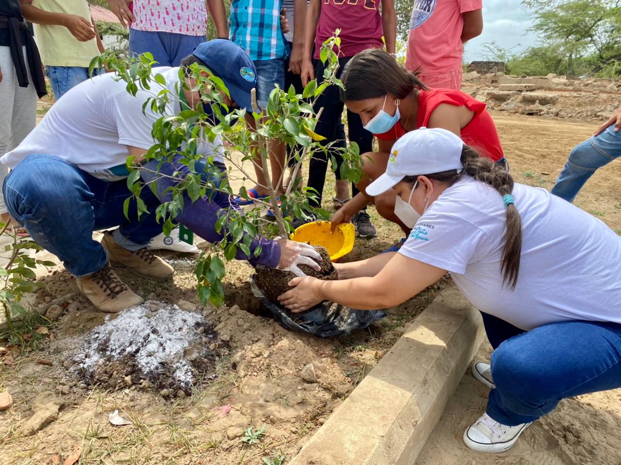 dos funcionarios de CORPAMAG con un miembro de la comunidad sembrando un arbol en el desarrollo de las actividades de educación